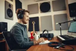 Musiker sitzt am Heimschreibtisch mit Interface und Laptop, nachdenklicher Blick, natürliches Licht