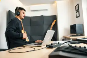 Musiker am Heimstudio-Schreibtisch vergleicht DHL, DPD und Hermes als Versandoptionen für Onlinehändler